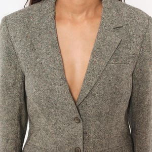 May include: A gray tweed blazer with a notched lapel and two buttons. The blazer has a tailored fit and a subtle flecked pattern in shades of gray, brown, and red. The jacket is a classic style.