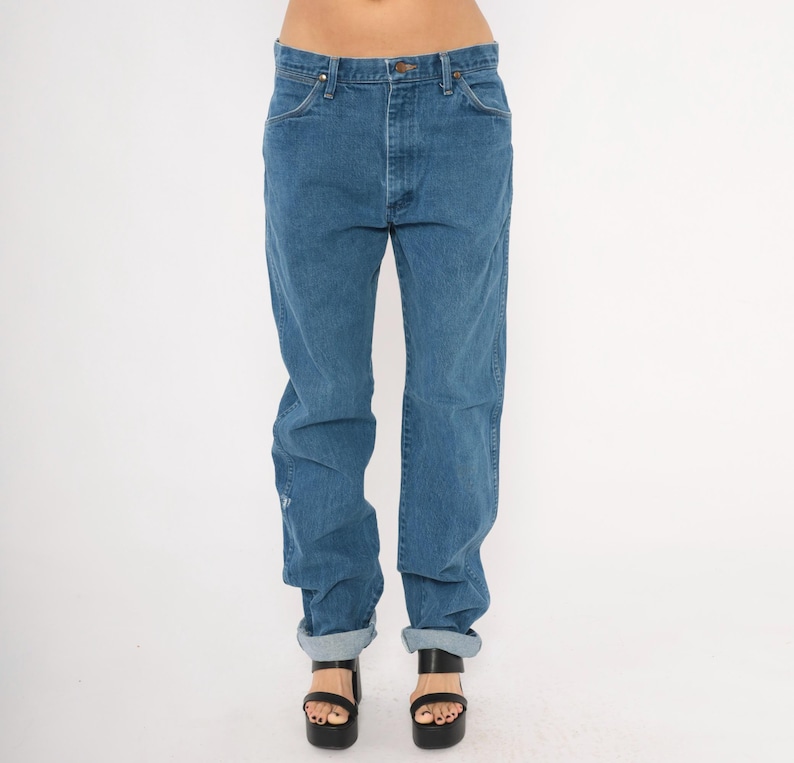 May include: Blue denim jeans with a classic fit. The jeans have a button and zipper closure, front and back pockets, and are cuffed at the ankles. The model is wearing black platform sandals. The jeans are a medium wash.