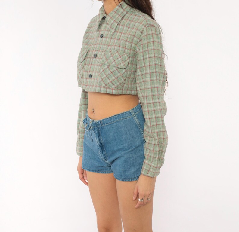 Puede incluir: Una camisa corta de manga larga con botones en un patr&oacute;n de cuadros verde claro y rojo, con cuello puntiagudo, dos bolsillos delanteros con solapa y botones oscuros, combinada con pantalones cortos de mezclilla azul de tiro alto.