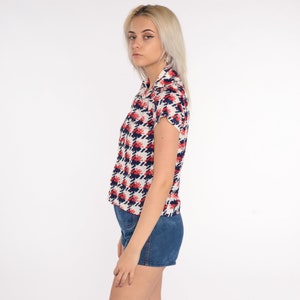 May include: A white button-down shirt with a red and blue geometric pattern. The shirt has short sleeves and a collared neckline.