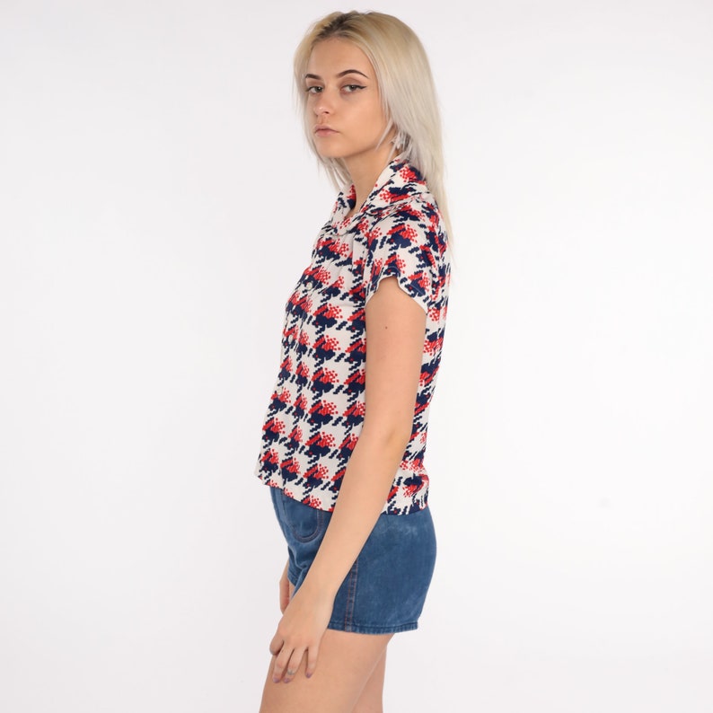 May include: A white button-down shirt with a red and blue geometric pattern. The shirt has short sleeves and a collared neckline.