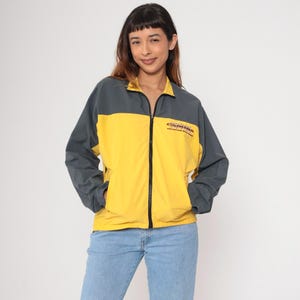 Pode incluir: Uma jaqueta corta-vento amarela e cinza com fecho de correr e o texto "Carolina Mountain Brewery" bordado na frente.