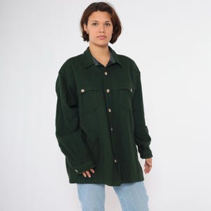 May include: A dark green long-sleeved shirt with a button-up front and two flap pockets. The shirt has a collar and is made of a soft, textured fabric.