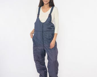 May include: Navy blue insulated snow bib overalls with adjustable straps and a full-length zipper. The quilted design provides warmth and protection from the elements. The overalls are designed for outdoor winter activities.