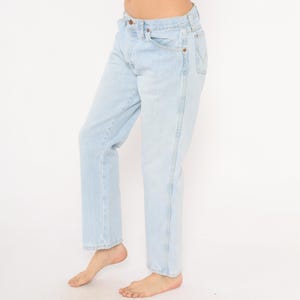 May include: Light blue denim jeans with a classic five-pocket design. The jeans have a straight leg fit and a button and zipper closure. The light wash denim is a faded blue color.