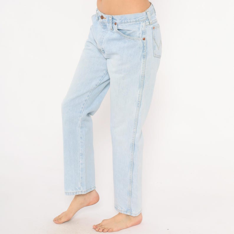 May include: Light blue denim jeans with a classic five-pocket design. The jeans have a straight leg fit and a button and zipper closure. The light wash denim is a faded blue color.