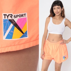 May include: A pair of bright orange athletic shorts with a TYR SPORT logo. The logo is a colourful geometric design with blue, yellow, pink, and black.