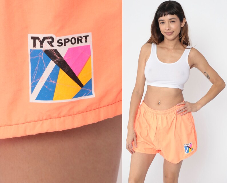May include: A pair of bright orange athletic shorts with a TYR SPORT logo. The logo is a colourful geometric design with blue, yellow, pink, and black.