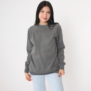 Op de afbeelding: Een grijs sweatshirt met een ronde hals en raglanmouwen.
