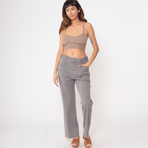 以下が含まれることがあります： 明るい茶色のクロップトップとグレーのチェック柄のパンツを着た女性。パンツはハイウエストでワイドレッグです。女性は茶色のサンダルを履いています。