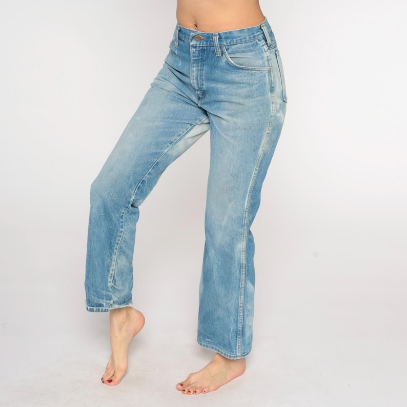 May include: Light blue denim jeans with a faded wash and a classic five-pocket design. The jeans have a straight leg fit and a button and zip closure. The denim has a worn look.