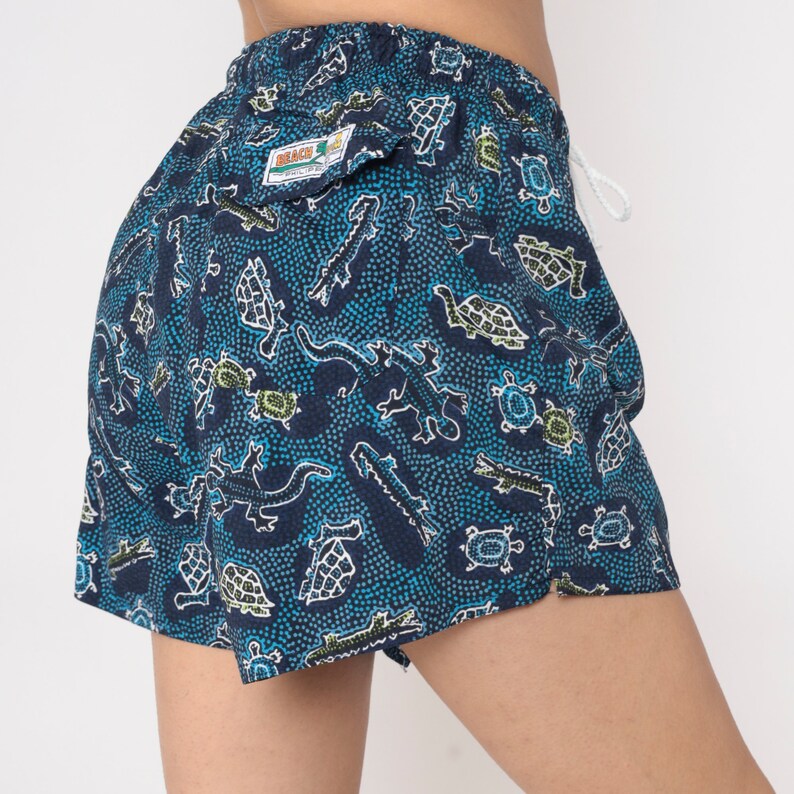 May include: Blue swim trunks with a white drawstring and a pattern of green and blue turtles, lizards, and snakes on a navy blue background. The brand name "Black & White" is printed on a white tag.