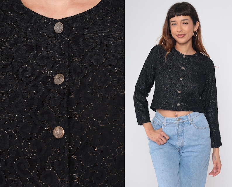 Puede incluir: Top negro de manga larga con estampado floral y botones redondos. El top es corto y tiene cuello redondo. Los botones son de color met&aacute;lico. La modelo lleva vaqueros azul claro.