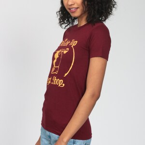 May include: A maroon t-shirt with a gold graphic of a drink and the text "The Double Top Malt Shop."
