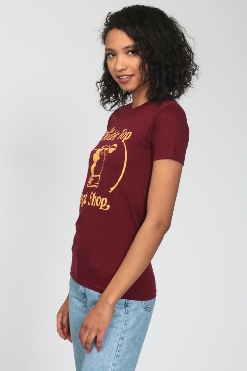 May include: A maroon t-shirt with a gold graphic of a drink and the text "The Double Top Malt Shop."