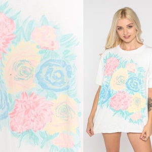 Puede incluir: Camiseta blanca con estampado floral pastel con rosas, margaritas y hojas.