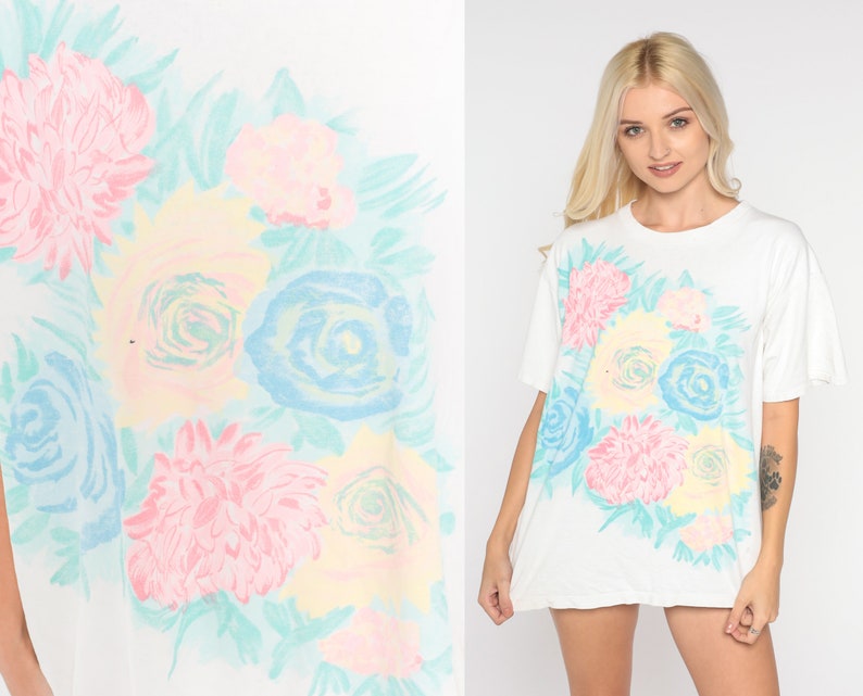 Puede incluir: Camiseta blanca con estampado floral pastel con rosas, margaritas y hojas.