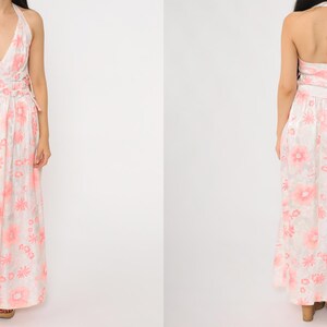 May include: A floor-length halter dress with a floral pattern in shades of pink and white. The dress features a V-neckline and a flowing skirt. The back of the dress is also visible, showcasing the halter tie and the continuation of the floral print.
