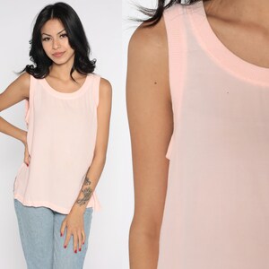 May include: A light pink sleeveless top with a round neckline. The top has a sheer overlay and a solid pink trim around the neckline and armholes. The fabric appears lightweight and suitable for warm weather.
