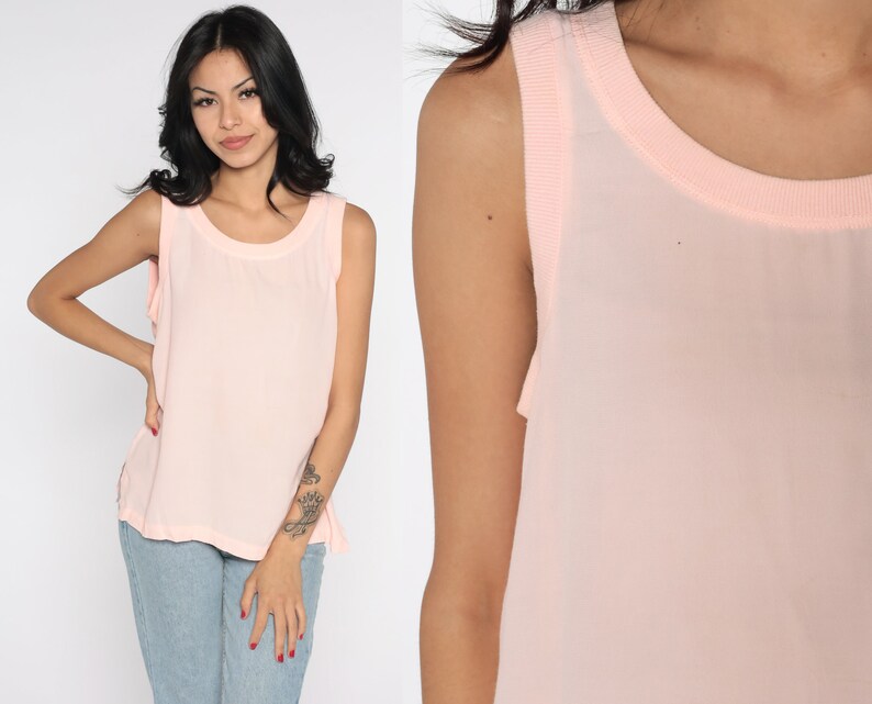May include: A light pink sleeveless top with a round neckline. The top has a sheer overlay and a solid pink trim around the neckline and armholes. The fabric appears lightweight and suitable for warm weather.