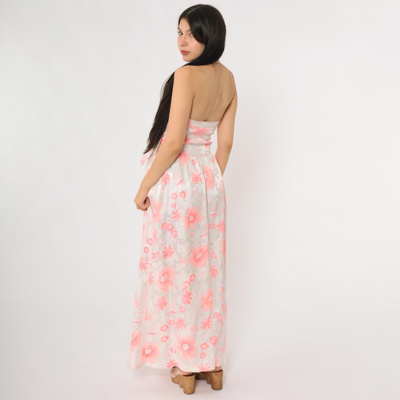 May include: A strapless, floor-length dress with a floral pattern in shades of pink and white. The dress features a fitted bodice and a flowing skirt. The model is wearing wooden platform heels.