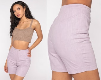 May include: A light purple pair of high-waisted shorts. The shorts have a button and zipper closure, and a tailored fit. The fabric appears to be a lightweight woven material. The shorts are shown with a brown crop top.