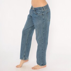 May include: Light blue denim jeans with a classic five-pocket design. The jeans have a straight leg fit and show slight distressing on the front. The jeans are worn by a person.