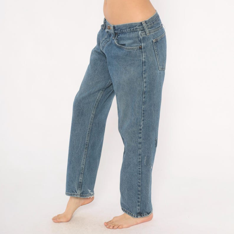May include: Light blue denim jeans with a classic five-pocket design. The jeans have a straight leg fit and show slight distressing on the front. The jeans are worn by a person.