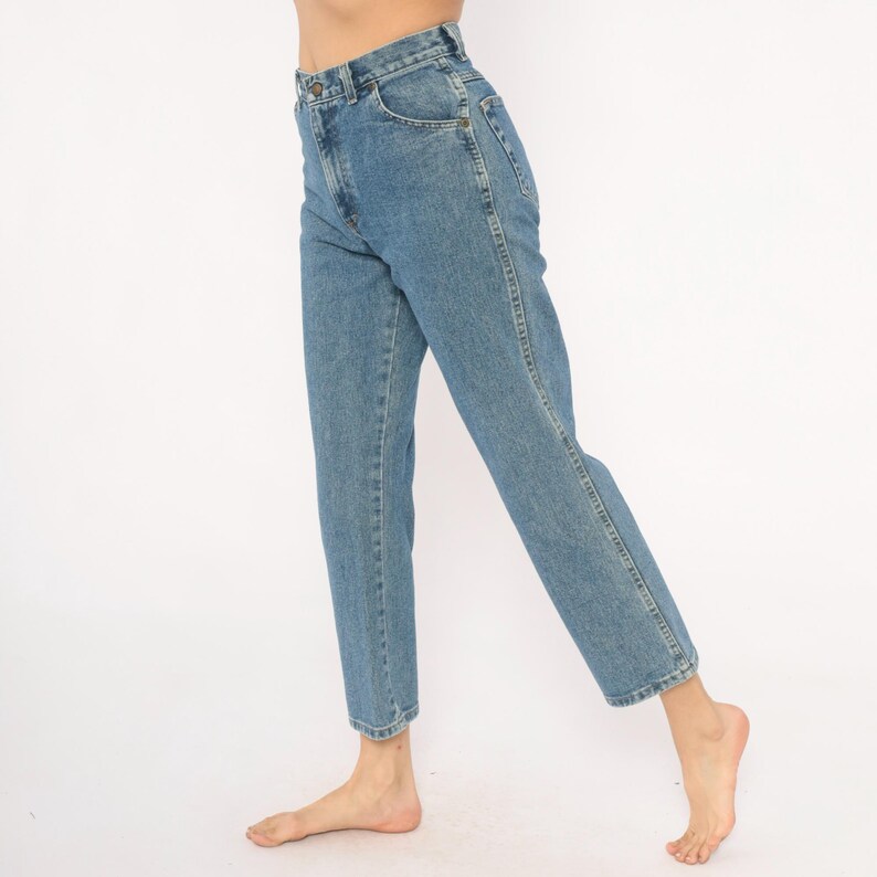 May include: Light blue denim jeans with a classic straight leg fit. The jeans have a button and zipper closure, front and back pockets, and a faded wash. The model is wearing the jeans with bare feet.
