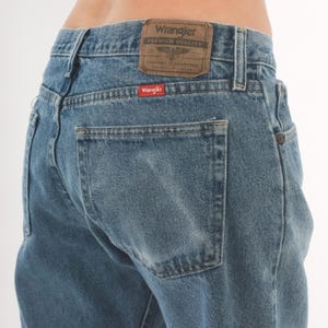 May include: Light blue denim jeans with a classic five-pocket design. The back features a Wrangler brand patch and a red Wrangler tag on the back pocket. The jeans have a straight leg cut.