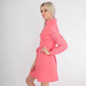 May include: A pink dress with a collared neckline and long sleeves. The sleeves are made of a sheer, patterned fabric. The dress has a fitted bodice and a flared skirt.