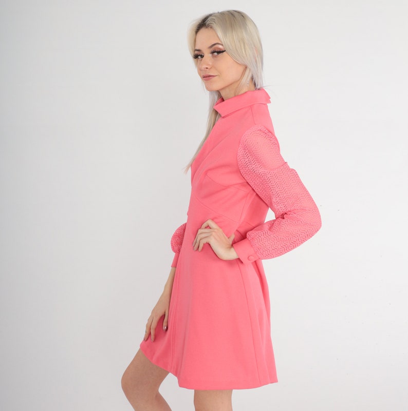 May include: A pink dress with a collared neckline and long sleeves. The sleeves are made of a sheer, patterned fabric. The dress has a fitted bodice and a flared skirt.