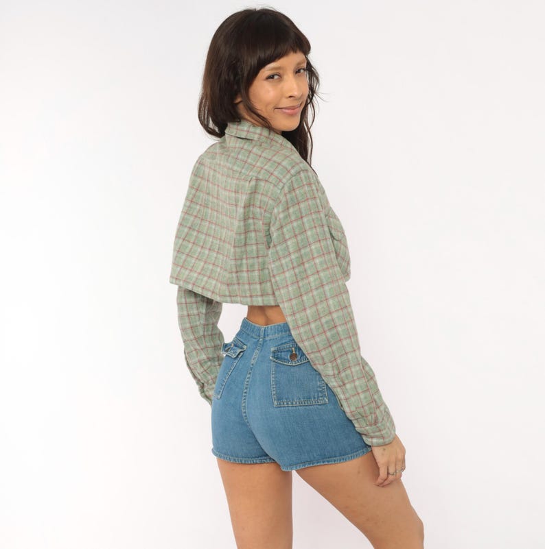 Puede incluir: Una camisa corta de manga larga con botones en un patr&oacute;n de cuadros verde claro y rojo, combinada con pantalones cortos de mezclilla azul de talle alto con dos bolsillos delanteros con cierre de bot&oacute;n y costuras visibles en la parte posterior.