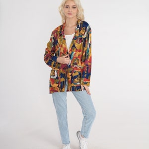 May include: A colorful, long-sleeved blazer with an abstract pattern in shades of red, yellow, blue, and brown. The blazer is worn over a white top and paired with light blue jeans and white sneakers. The overall style is casual and vintage.
