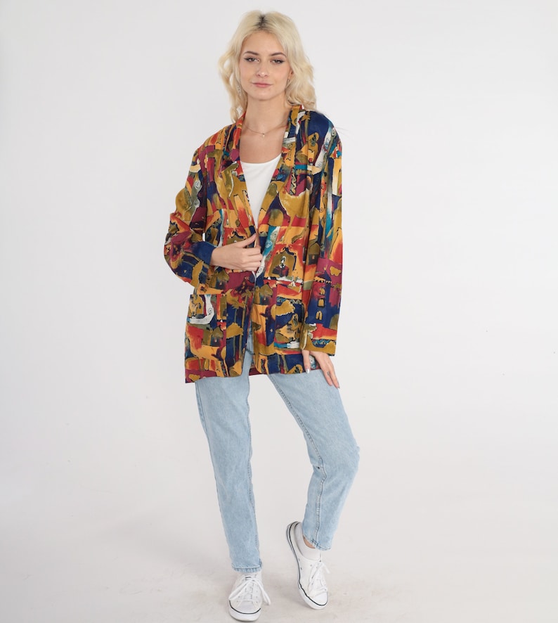 May include: A colorful, long-sleeved blazer with an abstract pattern in shades of red, yellow, blue, and brown. The blazer is worn over a white top and paired with light blue jeans and white sneakers. The overall style is casual and vintage.