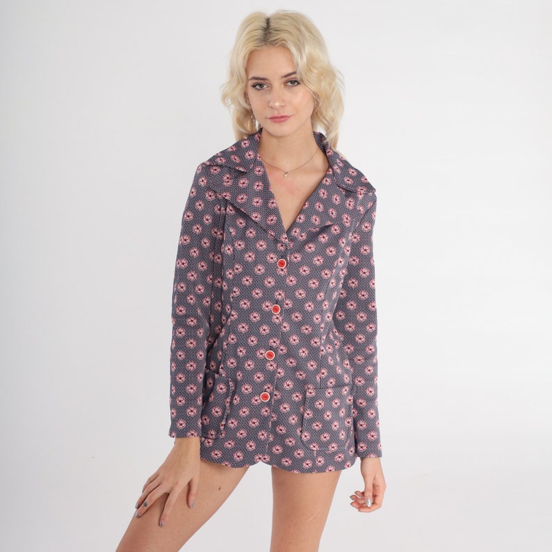 Puede incluir: Una chaqueta gris con estampado floral rosa y botones rojos. La chaqueta tiene cuello y mangas largas.