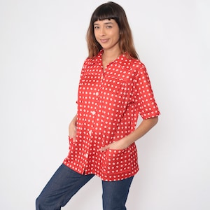 Könnte beinhalten: Ein rotes Hemd mit weißen Polka Dots. Das Hemd hat kurze Ärmel, zwei Vordertaschen und weiße Knöpfe. Das Model trägt eine blaue Jeans.