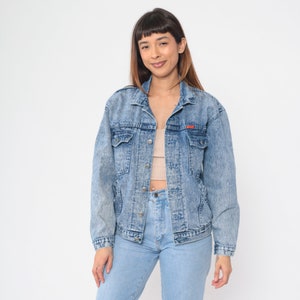 May include: A light blue denim jacket with a faded, distressed look. The jacket has a button-up front, two chest pockets, and two front pockets.