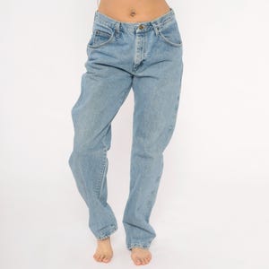 May include: Light blue denim jeans with a classic five-pocket design. The jeans have a relaxed fit and a straight leg, with a button and zipper closure. The jeans are made of a medium-weight denim fabric.