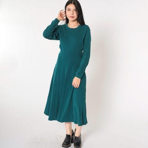 May include: A teal blue long-sleeved midi dress with a round neckline. The dress has a fitted bodice and a flowing skirt.