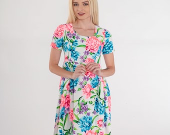 May include: A white dress with a floral print featuring pink, blue, and green flowers. The dress has a scoop neck and short sleeves.