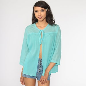 May include: A turquoise, open-front blouse with three-quarter sleeves. The blouse features a tie closure at the neckline and vertical pleats throughout the body. The sheer fabric adds a light and airy feel to the garment.