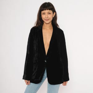 Puede incluir: Un blazer de terciopelo negro con cierre de un solo botón. El blazer tiene una solapa de muesca clásica y dos bolsillos delanteros. La modelo lleva vaqueros azul claro.