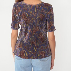 Puede incluir: Una camisa de manga corta azul y marr&oacute;n con un dise&ntilde;o plisado. La camisa tiene un cuello redondo y un corte holgado.