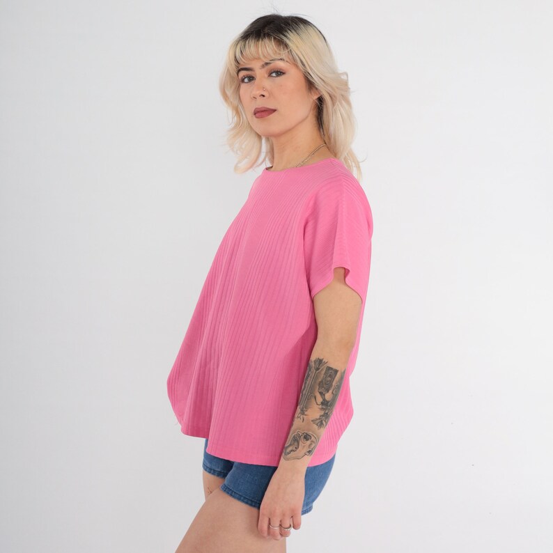 May include: A pink ribbed short-sleeved t-shirt with a round neckline. The shirt is loose-fitting and has a slightly cropped length.
