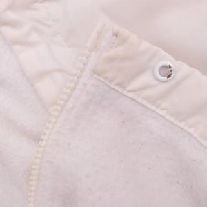 Puede incluir: Primer plano de una chaqueta blanca con forro polar. La chaqueta tiene cremallera y capucha. La tela es suave y texturizada. Se ve un ojal met&aacute;lico en la capucha.