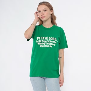 K&ouml;nnte beinhalten: Ein gr&uuml;nes T-Shirt mit dem wei&szlig;en Text: "PLEASE LORD... Let Me Prove To You That Winning The Lottery Won't Spoil Me." Das T-Shirt hat einen Rundhalsausschnitt.