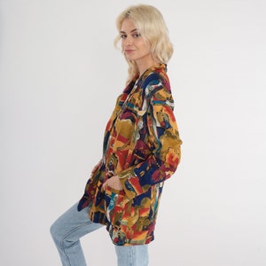 May include: A colorful blazer with an abstract pattern in shades of red, blue, yellow, and brown. The blazer has a classic lapel and long sleeves. The garment is worn with light blue jeans.