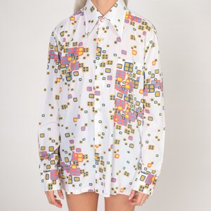 May include: A white long-sleeved shirt with a geometric pattern in shades of blue, yellow, pink, and brown.