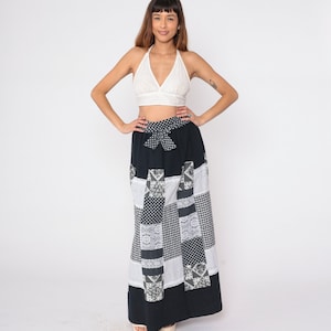 Peut inclure: Une jupe maxi patchwork noir et blanc avec un nœud blanc à la taille. La jupe est faite de différents tissus, dont du vichy, de la dentelle et des imprimés floraux.
